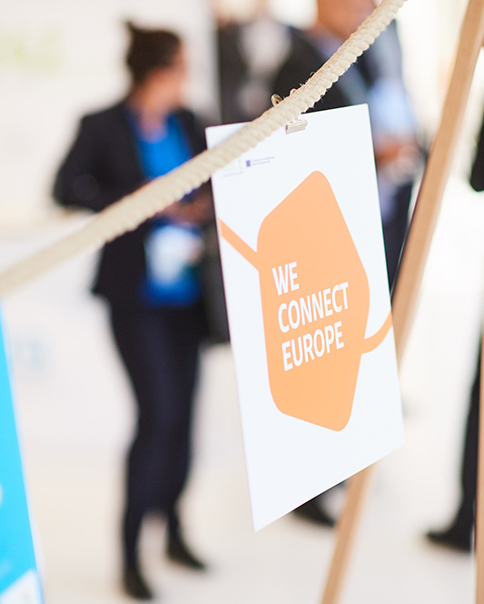 Personen betrachten eine Ausstellung zum Thema Elektromobilität. An einer Kordel hängt Papier mit dem Aufdruck WE CONNECT EUROPE
